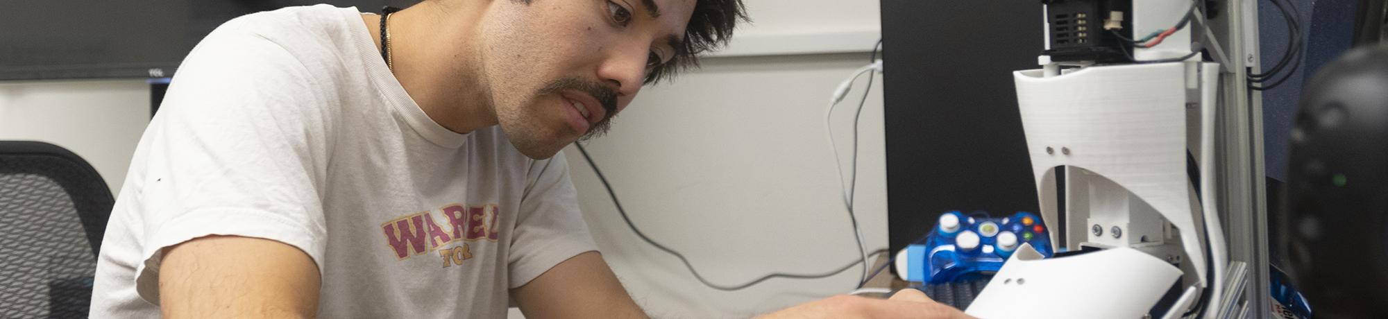 Male researcher at worktable examining a white plastic robotic prosthetic