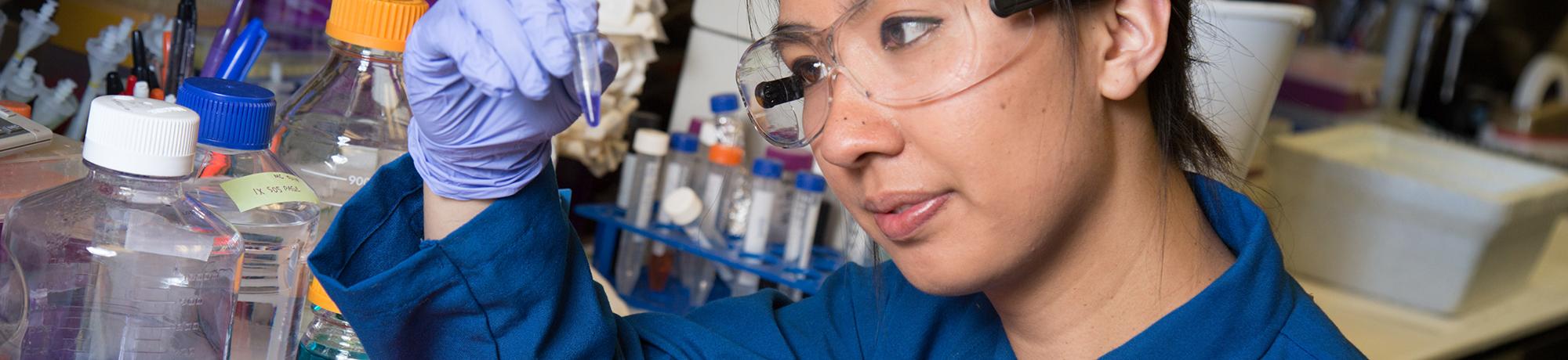 Female student in PPE examining a small vial